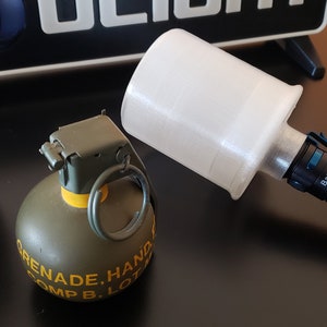 May include: An assortment of objects including two olive green hand grenades and a black and silver flashlight with a white diffuser. The grenades have yellow text and metal pins. The flashlight is labeled "Baton 3".