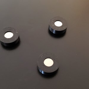 Könnte beinhalten: Drei schwarze runde Magnetplatten mit einem weißen Zentrum. Die Platten liegen auf einer schwarzen Oberfläche.