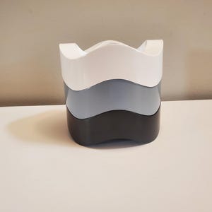 May include: A set of three nesting bowls in white, light blue, and black. The bowls have a wavy, organic shape.