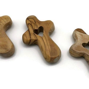 May include: Three wooden crosses with a heart cutout in the center. The crosses are made of olive wood and have a natural brown color.