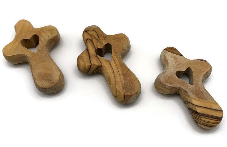 May include: Three wooden crosses with a heart cutout in the center. The crosses are made of olive wood and have a natural brown color.