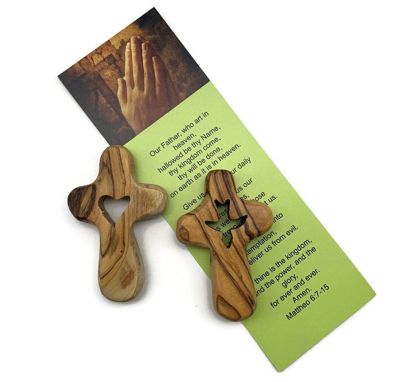 May include: Two wooden crosses with a heart and a dove cutout. The crosses are made of olive wood and have a natural wood finish. The crosses are accompanied by a card with the Lord's Prayer printed on it.