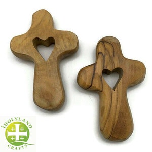 May include: Two small wooden crosses with a heart cutout in the center. The crosses are made of olive wood and have a natural brown color.