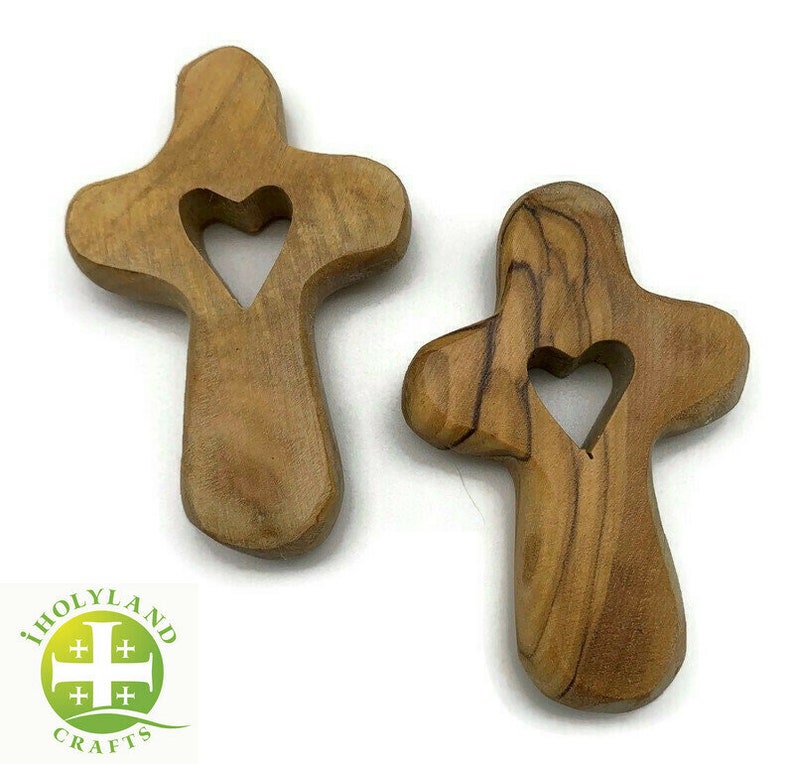 May include: Two small wooden crosses with a heart cutout in the center. The crosses are made of olive wood and have a natural brown color.