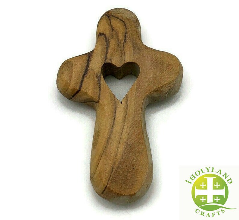May include: A wooden cross with a heart-shaped cutout in the center. The cross is made of olive wood and has a natural brown color.