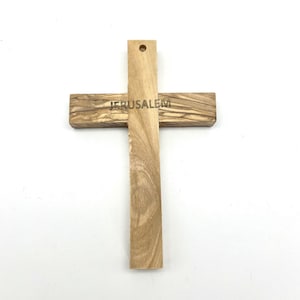 May include: A wooden cross with the word "JERUSALEM" engraved on the horizontal beam. The cross is made of light-colored wood with a visible grain pattern. It has a hole at the top for hanging.