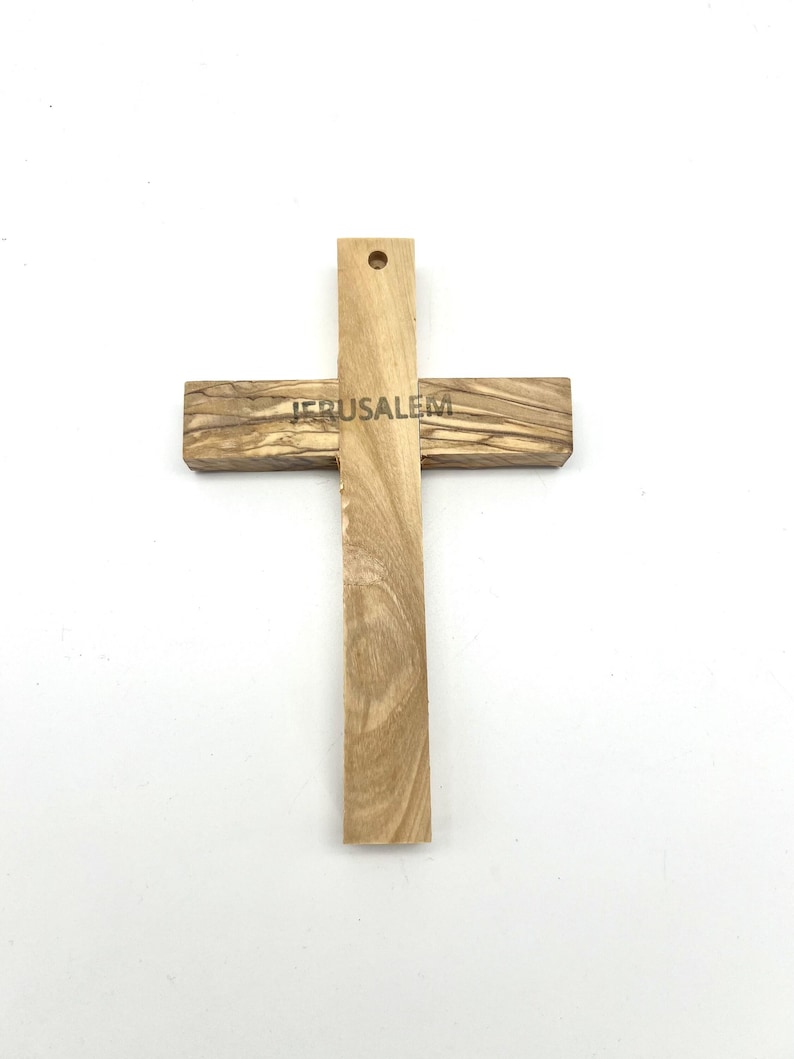 May include: A wooden cross with the word "JERUSALEM" engraved on the horizontal beam. The cross is made of light-colored wood with a visible grain pattern. It has a hole at the top for hanging.