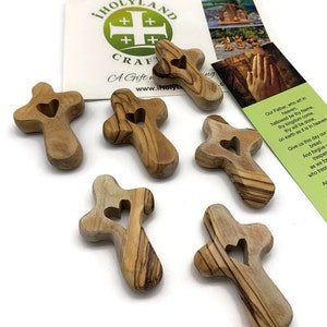 May include: Six small wooden crosses with a heart-shaped cutout in the center. The crosses are made of olive wood and have a natural wood finish.