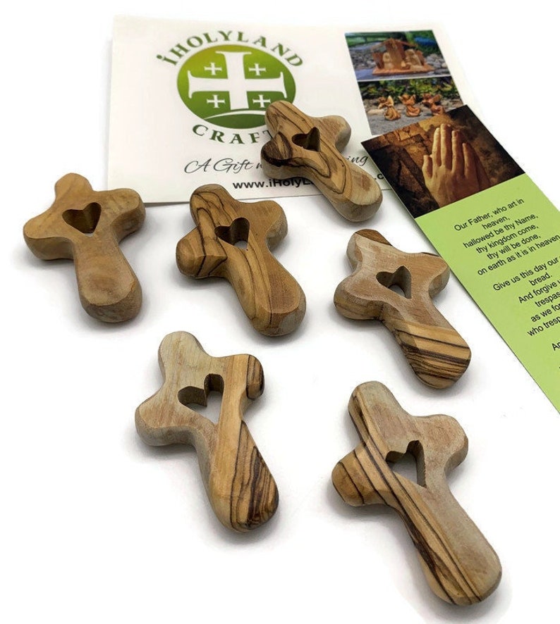 May include: Six small wooden crosses with a heart-shaped cutout in the center. The crosses are made of olive wood and have a natural wood finish.