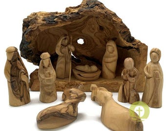 May include: A wooden nativity scene featuring carved figures of Mary, Joseph, baby Jesus, and other biblical characters. The figures are set inside a rustic wooden stable. The scene includes two wooden sheep. The figures are made of olive wood.