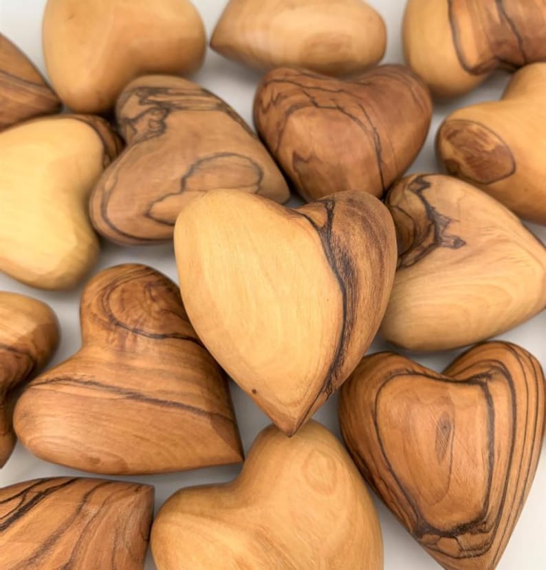 May include: A collection of multiple heart-shaped objects carved from light brown wood with visible dark brown grain patterns. Each piece features a smooth, polished surface and a distinct, rounded heart silhouette with natural wood variations.