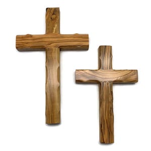 May include: Two wooden crosses with a natural wood grain finish. The crosses have a traditional Christian design, with a vertical beam intersected by a horizontal beam. The wood has a light brown color.
