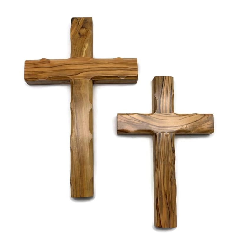 May include: Two wooden crosses with a natural wood grain finish. The crosses have a traditional Christian design, with a vertical beam intersected by a horizontal beam. The wood has a light brown color.