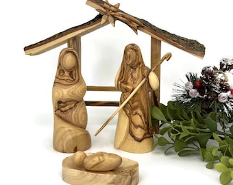 May include: A wooden nativity scene featuring carved figures of Mary, Joseph, and baby Jesus, along with a shepherd. The figures are under a rustic wooden shelter. The scene is made of light-colored wood with visible grain.