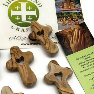 May include: Five small wooden crosses with a heart cutout in the center. The crosses are made of olive wood and have a natural wood finish. The crosses are arranged in a semi-circle on a white surface. The crosses are a religious symbol and are often used as a prayer aid.