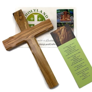 May include: A wooden cross with a natural wood grain finish. The cross is displayed with a bookmark featuring a prayer and the text "HOLYLAND" and "iHolyLandCrafts."