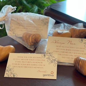 May include: Several smooth, polished olive wood hearts are displayed alongside two white rectangular cards. One card reads Always Near with a poem about loved ones, and the other card expresses gratitude from Gentiva. Some hearts are in sheer bags.