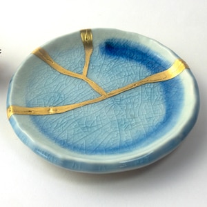 May include: A small, blue ceramic dish with gold accents. The dish has a crackled glaze and is perfect for holding jewelry or other small items.