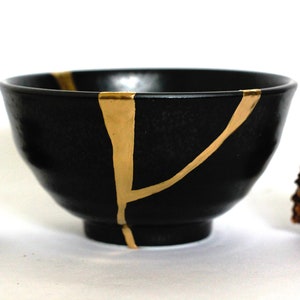 May include: A black ceramic bowl with gold crackle glaze. The bowl is round and has a wide rim. It is ideal for serving snacks or desserts.