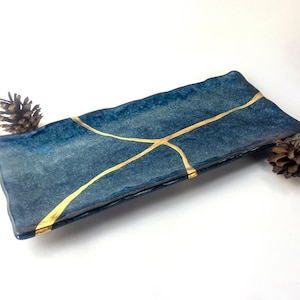 May include: A rectangular serving tray with a deep blue glaze and gold accents. The tray has a textured surface and a slightly wavy edge.