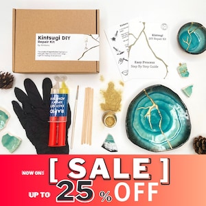 Può includere: Kit di riparazione Kintsugi DIY di Kinboru. Il kit include un adesivo epossidico bicomponente, foglia d'oro, applicatori in legno e un paio di guanti. Il kit è confezionato in una scatola marrone con il testo "Kintsugi DIY Repair Kit" e "by Kinboru". Il kit include anche istruzioni su come riparare la ceramica rotta con l'oro.