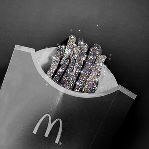 Może przedstawiać: Czarne opakowanie na frytki McDonald's z białym logo M, wypełnione grupą pionowych, patyczkowatych obiekt&oacute;w całkowicie pokrytych mieniącymi się, wielokolorowymi cyrkoniami, kt&oacute;re odbijają światło z niezwykłym blaskiem.