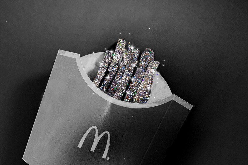 Może przedstawiać: Czarne opakowanie na frytki McDonald's z białym logo M, wypełnione grupą pionowych, patyczkowatych obiekt&oacute;w całkowicie pokrytych mieniącymi się, wielokolorowymi cyrkoniami, kt&oacute;re odbijają światło z niezwykłym blaskiem.