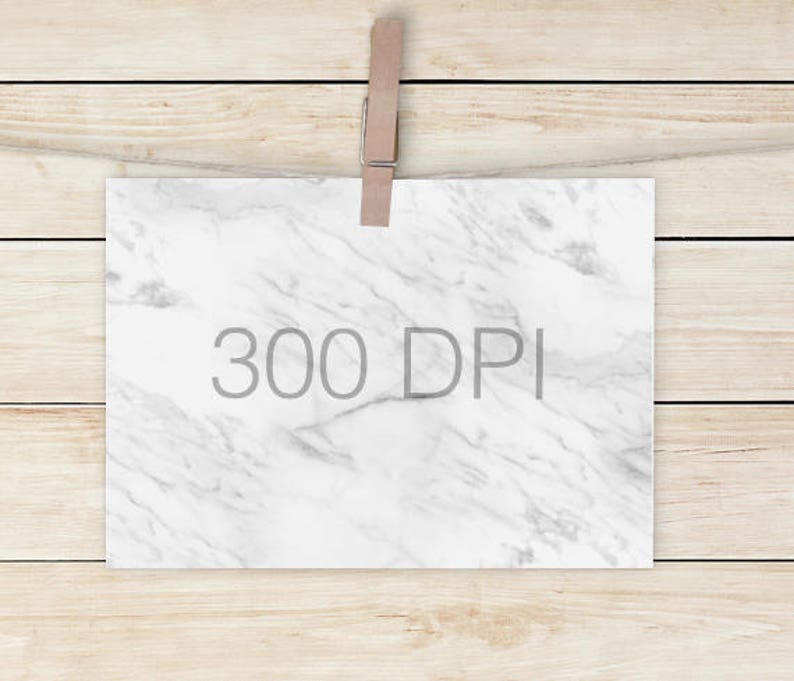 Puede incluir: Un papel blanco con un patr&oacute;n de m&aacute;rmol y el texto "300 DPI" en gris, sujeto por una pinza de madera en una cuerda. El fondo son tablas de madera de color marr&oacute;n claro.