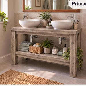 Könnte beinhalten: Ein rustikaler Badezimmerschrank aus Holz mit verwittertem grauen Finish, zwei weißen Keramik-Aufsatzwaschbecken und Chromarmaturen. Das Möbelstück verfügt über ein offenes unteres Regal mit grünen Handtüchern, einem Korb und Pflanzen.