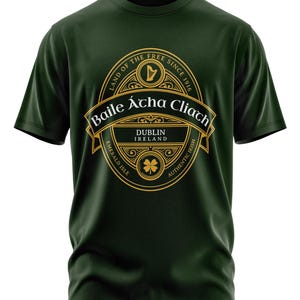 May include: A dark green t-shirt with a gold graphic design. The graphic features a stylized harp, the text "Land of the Free Since 1916", "Baile Átha Cliath", "Dublin Ireland", "Emerald Isle", and "Authentic Irish".