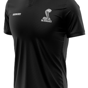 Puede incluir: Camiseta polo negra con un logotipo blanco bordado de Shelby Cobra en el pecho.