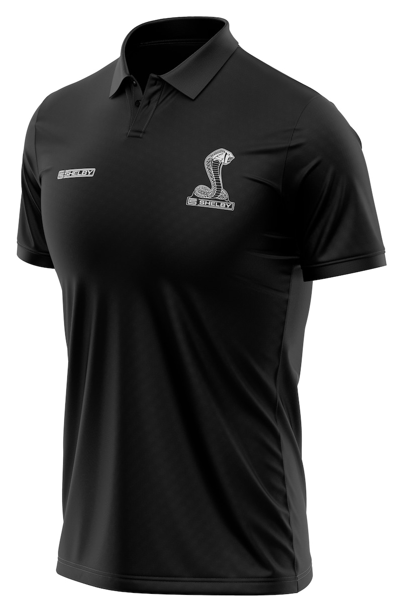 Puede incluir: Camiseta polo negra con un logotipo blanco bordado de Shelby Cobra en el pecho.