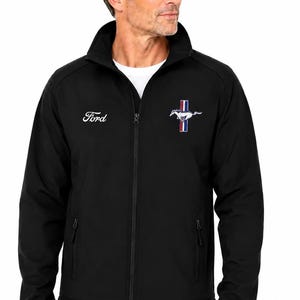 Peut inclure: Une veste noire zippée avec le logo Ford blanc sur la poitrine droite et l'emblème du cheval Ford Mustang avec des bandes verticales rouges, blanches et bleues sur la poitrine gauche. La veste a un col montant, des manches longues et deux poches.