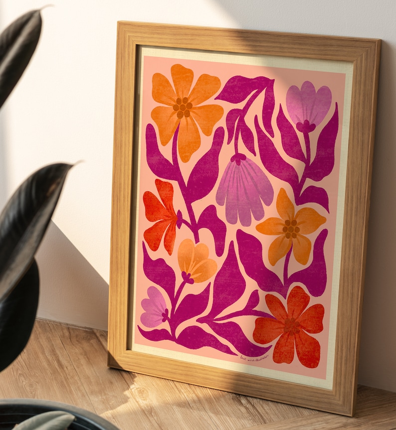 May include: A framed print with a pink background featuring a floral design with orange, red, and purple flowers. The flowers are stylized and have a retro feel. The print is framed in a light wood frame.