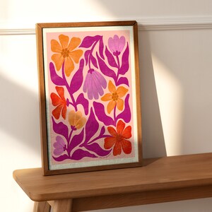 May include: A framed print with a pink background and a colorful floral pattern. The flowers are in shades of orange, pink, and purple. The print is in a wooden frame.