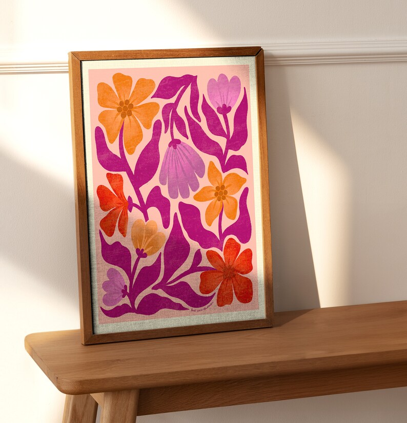 May include: A framed print with a pink background and a colorful floral pattern. The flowers are in shades of orange, pink, and purple. The print is in a wooden frame.