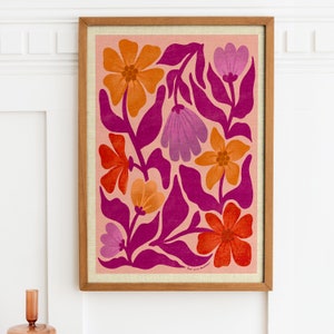May include: A framed print with a floral design featuring pink, orange, and red flowers on a light pink background. The print has a pink and white floral pattern with a pink background. The print is framed in a natural wood frame.