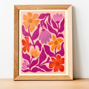 May include: A framed print with a pink background and a floral pattern in shades of orange, pink, and red. The flowers are stylized and have a retro feel. The print is signed "but we thrive" in the bottom right corner.