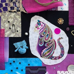 May include: A purple and gold cat illustration on a white background surrounded by various fabric scraps, lace, and embellishments. The fabric scraps are in shades of purple, pink, blue, and white. The embellishments include beads, buttons, and a gold tassel.