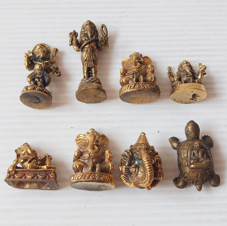 A collection of various small brass Ganesha amulets in different poses and one brass turtle amulet, handcrafted divine remover of obstacles for success and prosperity. Price per one piece.