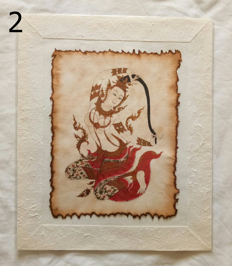 May include: A framed print of a traditional Thai painting depicting a woman in a red and gold dress, holding a black ribbon. The painting is on aged paper with a textured border.
