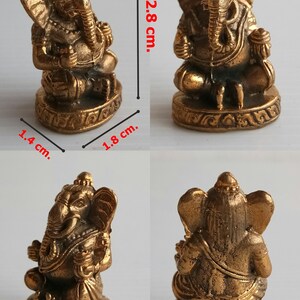 Może przedstawiać: Mała, brązowa statua hinduskiego boga Ganeshy, siedzącego w pozycji medytacyjnej. Statua ma 2,8 cm wysokości, 1,8 cm szerokości i 1,4 cm głębokości. Podstawa jest misternie zdobiona. Obraz jest oznaczony jako "Ganesh 3".