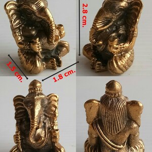 Może przedstawiać: Mała, brązowa statua Ganeshy. Figurka ma 2,8 cm wysokości, 1,8 cm szerokości i 1,5 cm głębokości. Statua przedstawia hinduskie b&oacute;stwo Ganeszę w pozycji siedzącej, ze skomplikowanymi detalami.