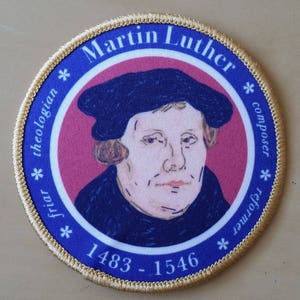 Può includere: Una toppa rotonda con bordo dorato, sfondo blu e un ritratto di Martin Lutero. Il testo "Martin Lutero" è scritto in un arco dorato nella parte superiore della toppa. Il testo "frate * teologo * compositore * riformatore" è scritto in un cerchio dorato attorno al ritratto. Il testo "1483 - 1546" è scritto in un arco dorato nella parte inferiore della toppa.