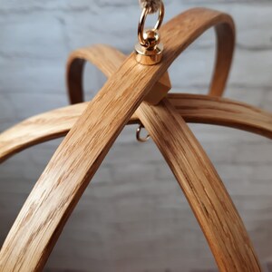 May include: A wooden mobile hanger with a gold metal hook and ring. The hanger is made of natural wood and has a rustic look.