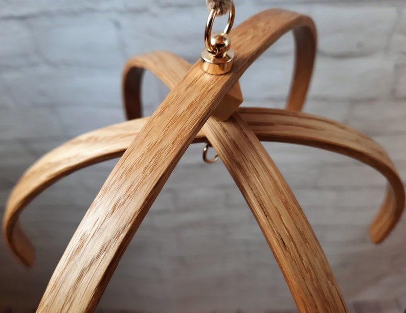 May include: A wooden mobile hanger with a gold metal hook and ring. The hanger is made of natural wood and has a rustic look.