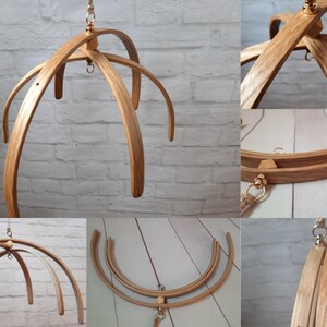 May include: A wooden baby mobile frame with four curved arms, made of natural wood with a light brown finish. The frame is suspended from a gold-colored hook and has a gold-colored ring at the top.