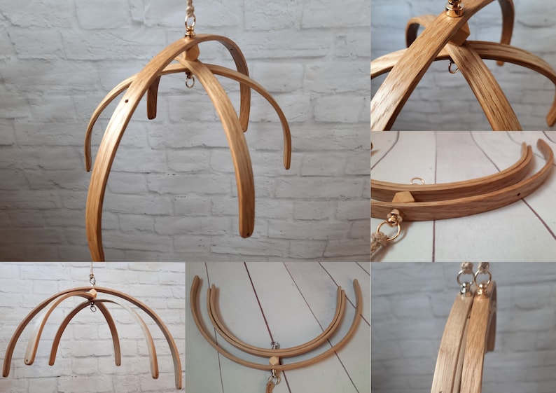 May include: A wooden baby mobile frame with four curved arms, made of natural wood with a light brown finish. The frame is suspended from a gold-colored hook and has a gold-colored ring at the top.