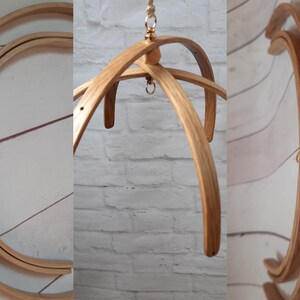 May include: A wooden baby mobile frame with three curved wooden arms and a gold metal hook at the top. The frame is made of natural wood and has a rustic look.