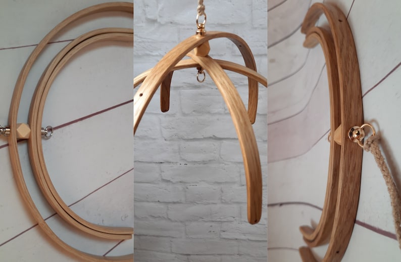 May include: A wooden baby mobile frame with three curved wooden arms and a gold metal hook at the top. The frame is made of natural wood and has a rustic look.